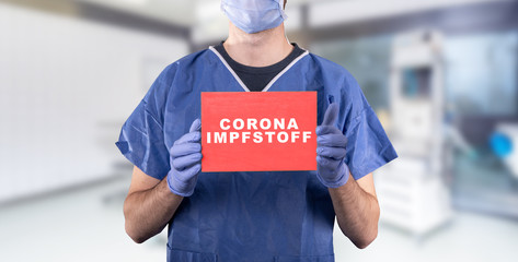 Arzt mit Schild auf dem Corona Impfstoff steht, Krankenhaus Hintergrund