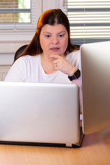 Professional woman working at home. She has two computers on her desktop and is concentrated to...