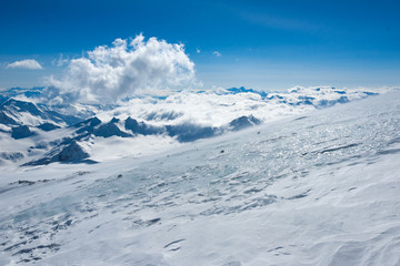 High mountains view with naked ice surface of the glacier in sunlight on the front and summits in clouds on the back