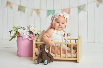 Cute funny baby with bunny ear. Easter greeting card, copyspace for your text. Poster for Easter holiday. Easter bunny. Congratulations on Mother's Day. Easter rabbit. Cute baby girl 6 months in bed