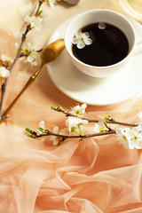 Beautiful spring still life with white cup of hot coffee or tea, peach-colored tulle, golden spoon...