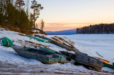 Abandoned fishing boats on the lake in winter at sunset