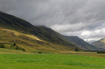 Fototapeta na wymiar Sun breaking through the dark Cloud layer and on to the shadowed slopes of the Valley sides of Glen Clova on an August Morning,