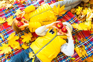 Happy children lying on fall leaves in autumn park with apples.