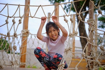 A cute Asian girl playing in a wooden and twine obstacle course for kids, happy and smiling.