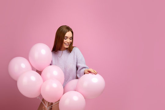 Smiling attractive girl posing with pastel pink air balloons isolated over pink background. Beautiful happy young woman on a birthday holiday. space for text