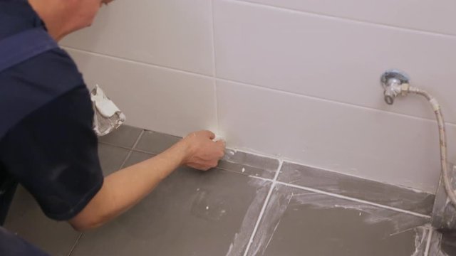 Worker troweling joints between tiles on floor