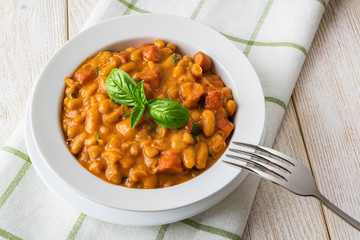 Backed beans with sausage slices in tomato sauce and parsley in a white bowl with fork on a wooden table. Source of vegetable protein and ingredient for vegetarian food.