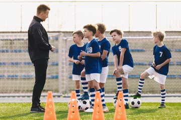 Young coach explaining training rules to children school soccer team. Kids in football team listening to coach. Boys on soccer practice. Physical education outdoor class - obrazy, fototapety, plakaty