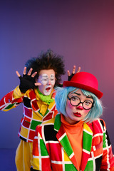 Two clowns a man and a woman with makeup in bright colored costumes are fooling around and showing a presentation