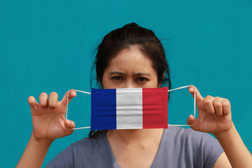 A woman with France flag on hygienic mask in her hand and lifted up the front face on light blue color background. Tiny Particle or virus corona or Covid 19 protection.