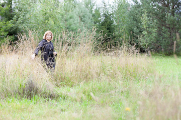 Birds watcher coming from dry grass, mature woman with binoculars in hand, natural scientist, copyspace