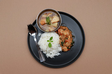 Breakfast in the black round plate on the brown floor. Minced pork and shrimp with basil fried with rice and soup in cup.