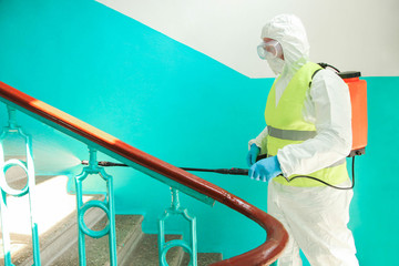 A specialist in a protective suit disinfects the railing