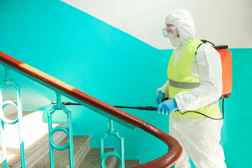 Naklejka premium A specialist in a protective suit disinfects the railing