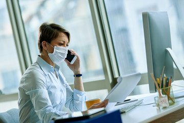 Businesswoman with face mask reading reports and talking on cell phone in the office.