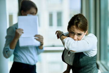 Young businesswoman sneezing into elbow in the office.