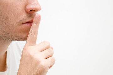 Young man finger showing shush gesture. Sign for silence. Face closeup. Isolated on light gray background. Empty place for text, quote or sayings. Side view.