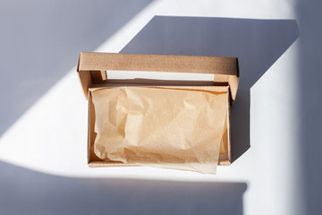 Kraft cardboard post parcel with natural sunlight shadow on white background in creative minimalism style.Brown eco gift box, online shopping concept.Shop super sales,discount tag special offer banner