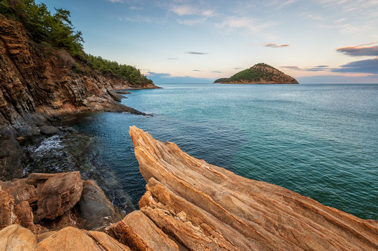 Magnificent sunset view at the rocky coastline of Thasos island and view to little island Nisida Kinira, Greece