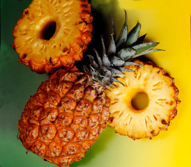 Whole pineapple and two slices of pineapple with the rind on a yellow background