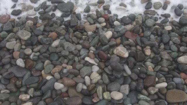 Sea waves roll on pebbles shore during a light storm close up top view