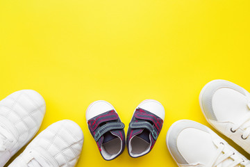 Father, mother and little kid shoes on bright yellow table background. Sport together concept. Top...