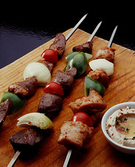 Skewers of poppy, meat and hearts on an industrial wooden bedding and a hummus dish next door