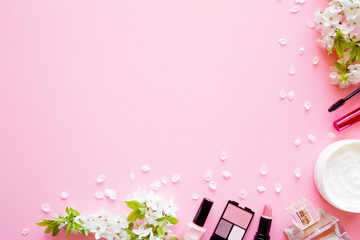 Various decorative makeup cosmetics with herbal cream jar and fresh cherry blossoms and petals on pink table background. Pastel color. Empty place for text. Flat lay. Top down view.