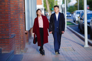Asian girl and guy are walking in the autumn city and holding hands. They are smiling and very happy to be together. Bright and beautiful photo