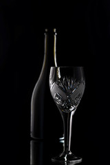 A bottle of wine and a crystal wine glass on a black background.