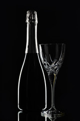 A bottle of wine and a crystal wine glass on a black background.
