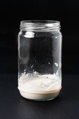 Food concept Making a homemade Sourdough Starter or leaven yeast fermented mixture of flour and water in glass jar on black slate stone board