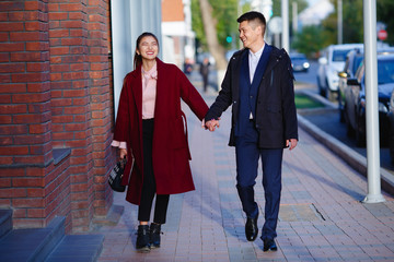 Asian girl and guy are walking in the autumn city and holding hands. They are smiling and very happy to be together. Bright and beautiful photo