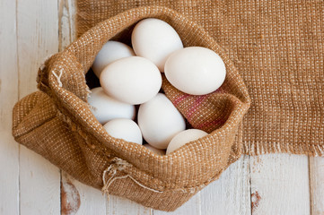 White chicken eggs lying in a canvas bag, shot on a white painted wooden surface. Background for livestock products.