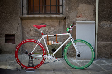 Fototapeta na wymiar Colored bicycle - red and green, in front of the facade of an old house in empty street background.