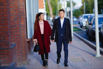 Asian girl and guy are walking in the autumn city and holding hands. They are smiling and very happy to be together. Bright and beautiful photo