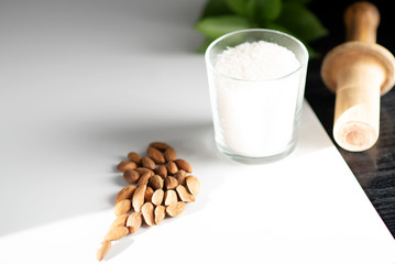 coconut flakes in a glass and sprinkled almonds on a white background, with a green leaf of a plant.