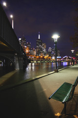 Night of autumn in Melbourne city with skyline bench and street lamp beside the Yarra river