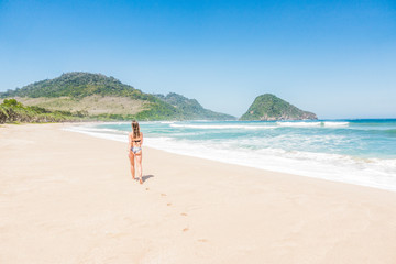 Fototapeta na wymiar Young attractive woman in bikinis walking on an empty wild tropical beach on a sunny summer day.