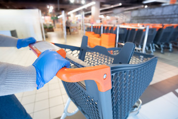 Hands in glives with a shopping cart at a supermarket. Grocery shopping, buying essential food at quarantine or covid-19 epidemic - obrazy, fototapety, plakaty
