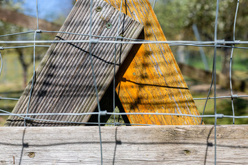Drewniny plot i siatka. Ogrodzenie dzialki.  Zabudowa wiejska. Brozowe i pomaranczowe deskiw plocie. Powiekszenie desek.  Drewniane elementy konstrukcyjne.   © ff25