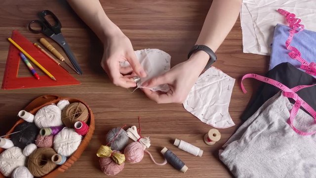 Hands of a young caucasian woman in a sewing thimble from white cotton fabric at night in the house. Making your own reusable protection masks. Close-up view of a woman's hands. Top view