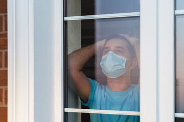 Sad man in a medical mask look at the window