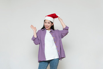 A young asian woman in a Christmas hat stands in front of the white wall