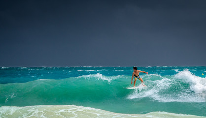 Surfeur sur une vague turquoise et ciel menaçant