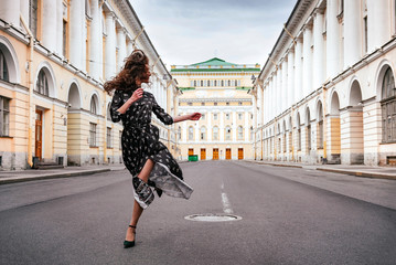 1 white young beautiful woman in a long dress walking along the road on the street in the background of a building - Powered by Adobe