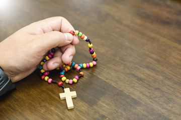 Closeup of catholic rosary beads in hand on wooden table.