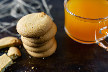 Homemade shortbread, round-shaped pastry on a dark old surface in a stack of crumbs. Next to it is a glass mug with orange mulfruit juice