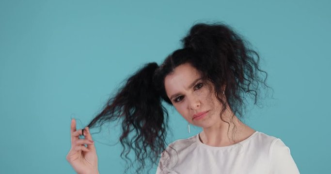 Portrait of beautiful young woman with black curly hair chewing bubble gum play with hair in front of blue background shot in 4k super slow motion